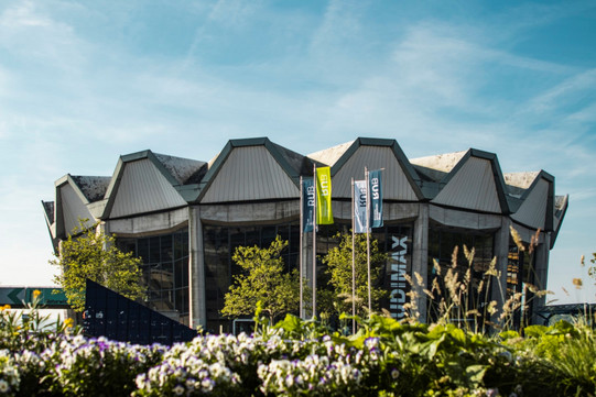 Die AudiMax der RUB steht vor einem blauen Himmel mit blühenden Blumen im Vordergrund.