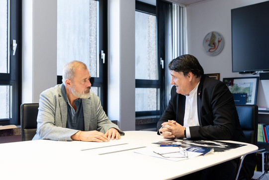 Friedensnobelpreisträger Dmitry Muratov im Gespräch mit RUB-Rektor Martin Paul an einem Konferenztisch. Beide sitzen einander gegenüber in einem hellen Büro, auf dem Tisch liegen Unterlagen.